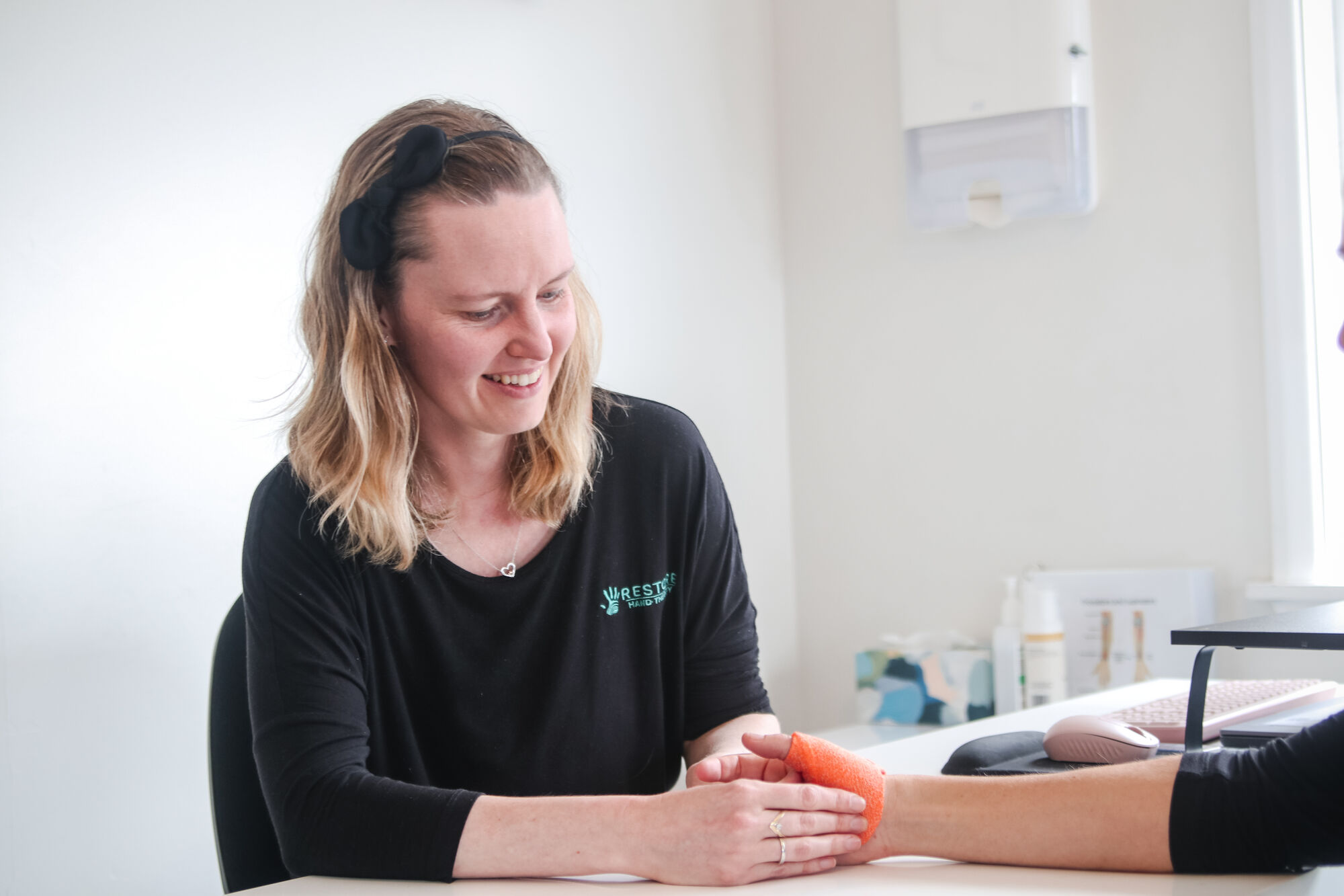 A Restore hand therapist smiling as she supports a patient's hand in a custom orange splint